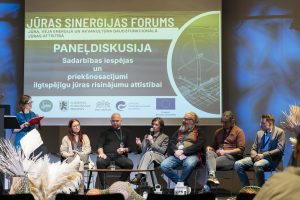 Paneļdiskusijā eksperti apspriež sadarbības iespējas un ilgtspējīgu jūras risinājumu attīstību Baltijas jūras reģionā. Uz skatuves redzami dažādu nozaru pārstāvji, auditorija seko līdzi diskusijai.