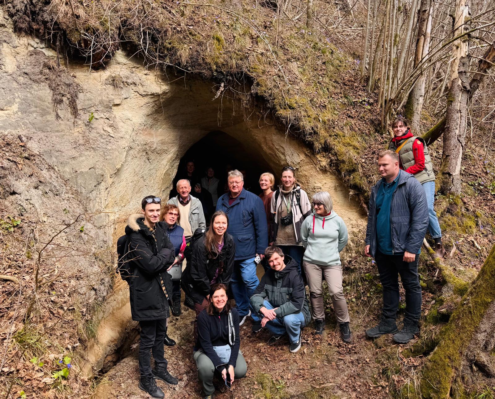 Apmācību dalībnieki Abavas ielejā pie smilšakmens atseguma klausās pasniedzēja skaidrojumu par iežu slāņiem un to veidošanās procesiem, vērojot dabas piemērus vidē.