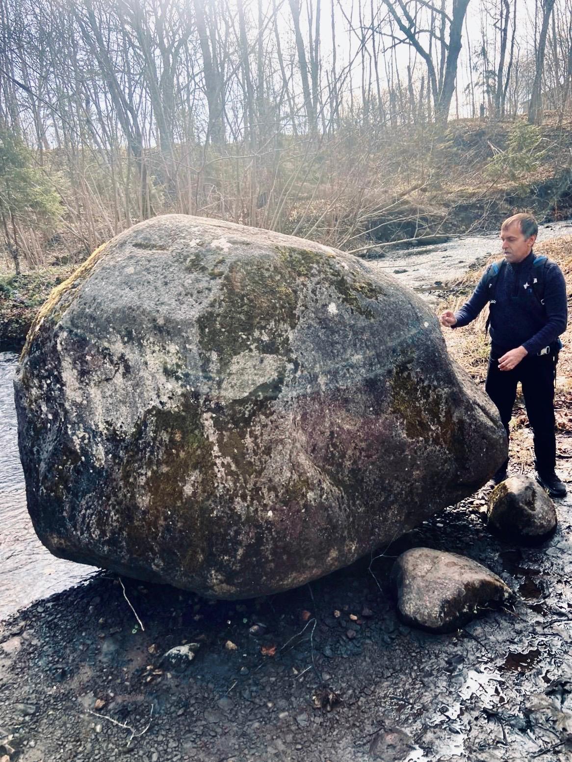 Apmācību laikā dalībnieki dabā pēta lielu laukakmeni upes krastā, kur pasniedzējs skaidro ledāju darbības ietekmi un iežu pārvietošanās procesus.
