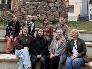 Projekta partneru grupa sēž pie vēsturiskas ēkas mūra sienas, piedaloties pieredzes apmaiņas pasākumā Igaunijā par pieejamības risinājumiem tūrisma objektos.