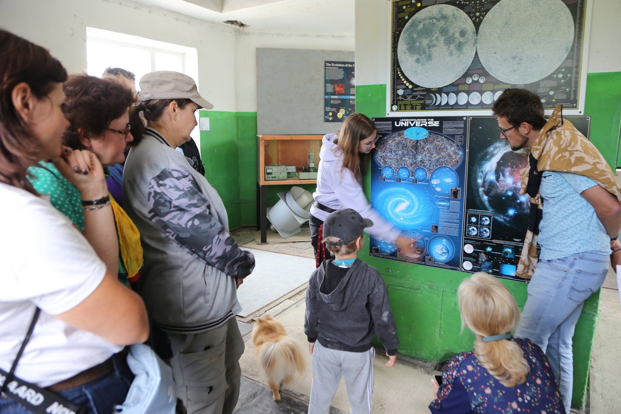 Dalībnieki Irbenes radioteleskopa ekspozīcijā iepazīst plakātus par Visumu un astronomijas izpēti.