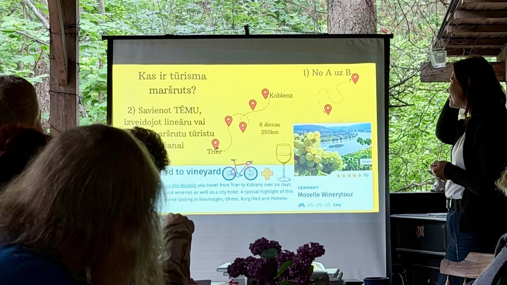 Lektore darbnīcā skaidro, kas ir tūrisma maršruts, rādot piemēru ar tematisku vīna tūres maršrutu.