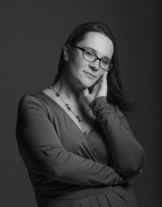 Melnbalts studijas portrets: ērģelniece Iveta Pelše brillēs, ar roku atbalstījusi vaigu un mierīgi raugās kamerā.