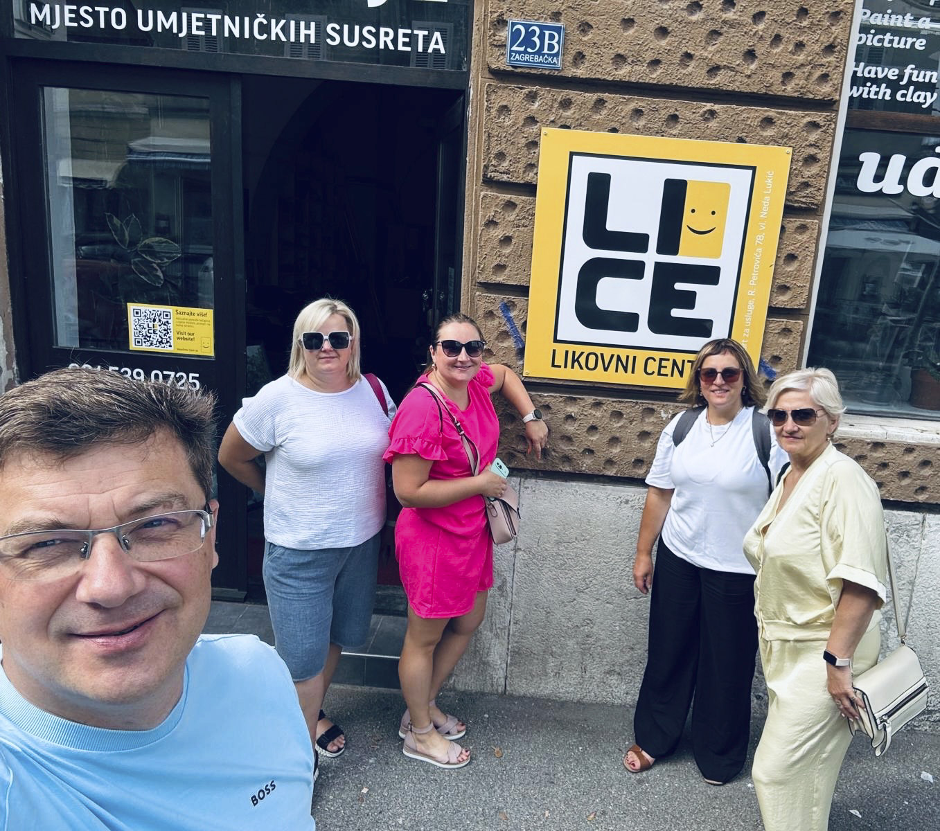 Pieci mobilitātes dalībnieki saulainā dienā smaida kopīgā pašportretā pie mākslas centra “Lice” ieejas Zagrebā.